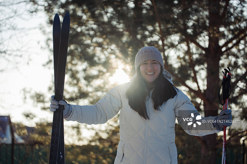 在阳光明媚的冬日，乡村里，兴奋的女子拿着滑雪板和滑雪杖。图片素材