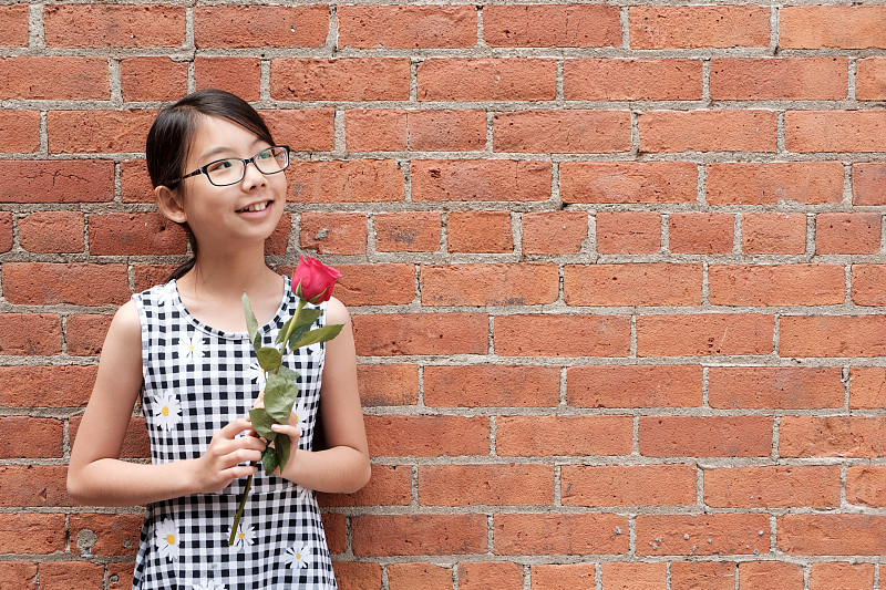 年輕的亞洲女孩的肖像與紅玫瑰花靠在紅色磚墻圖片素材
