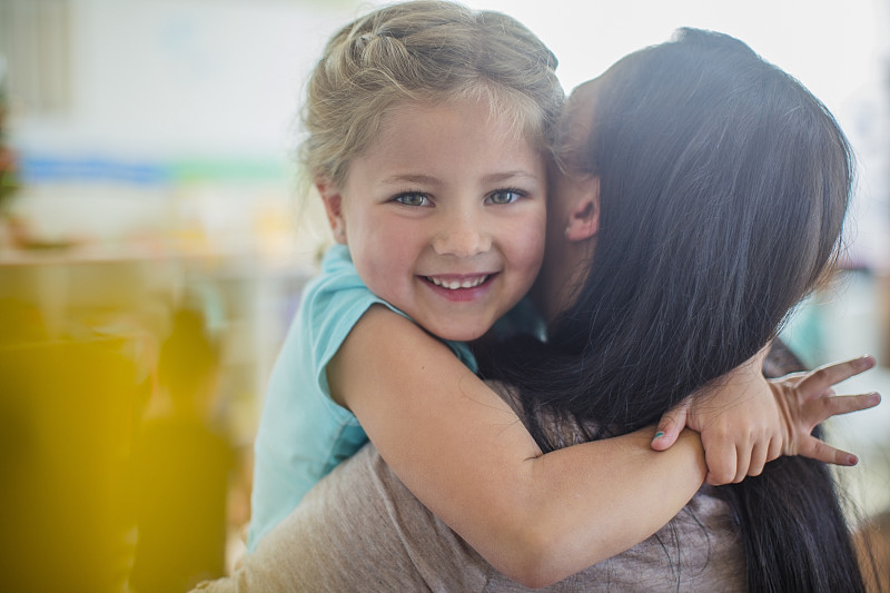 微笑的女孩在幼兒園擁抱學前班老師的肖像圖片素材