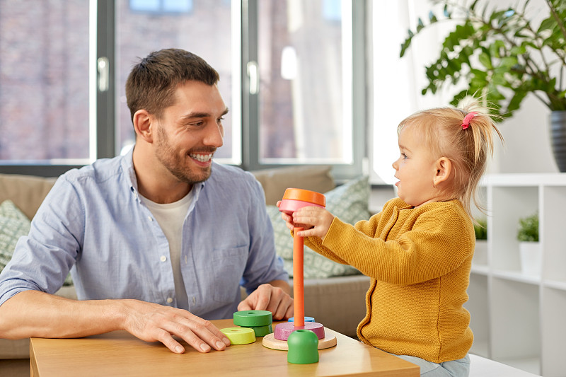 家庭，父親和人的概念-快樂的父親和小寶貝女兒在家里玩金字塔玩具。爸爸在家里和小女兒玩圖片素材