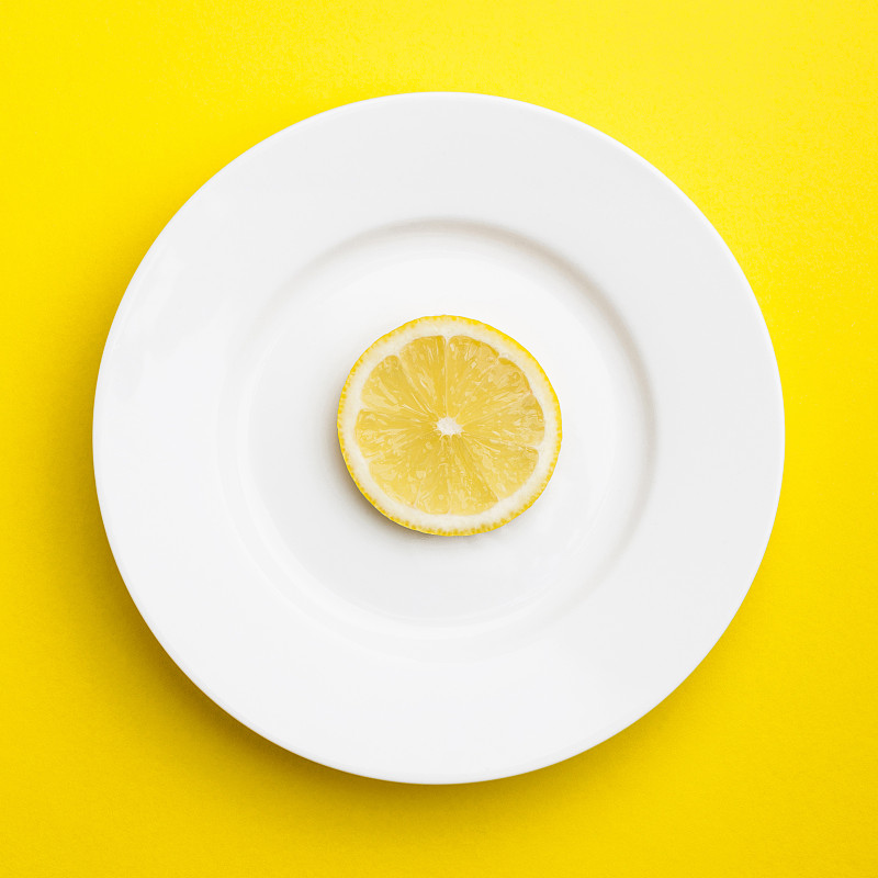 在馬來西亞吉隆坡，一片檸檬躺在白色的盤子上，黃色的背景圖片素材