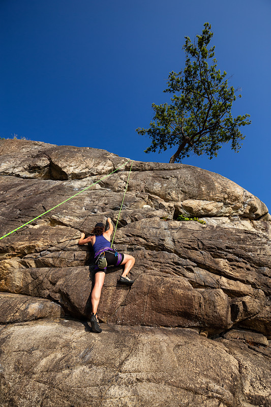 低角度的女人爬在巖石上對清澈的藍色天空圖片素材