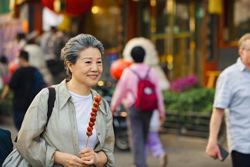 老年人City walk系列:老年女人拿着糖葫芦在北京什刹海胡同商业街旅行图片下载