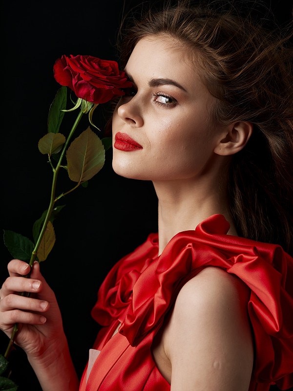 浪漫的女人穿著紅色的套裝，拿著一朵鮮紅的玫瑰。圖片素材