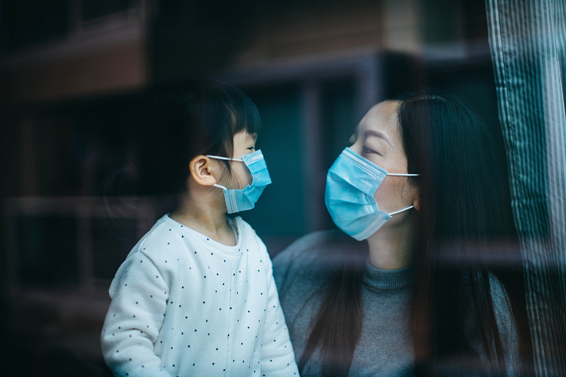 新冠肺炎疫情爆發，年輕的母親和小女兒戴著防護口罩，在家中自我隔離，以保護和防止病毒傳播圖片素材