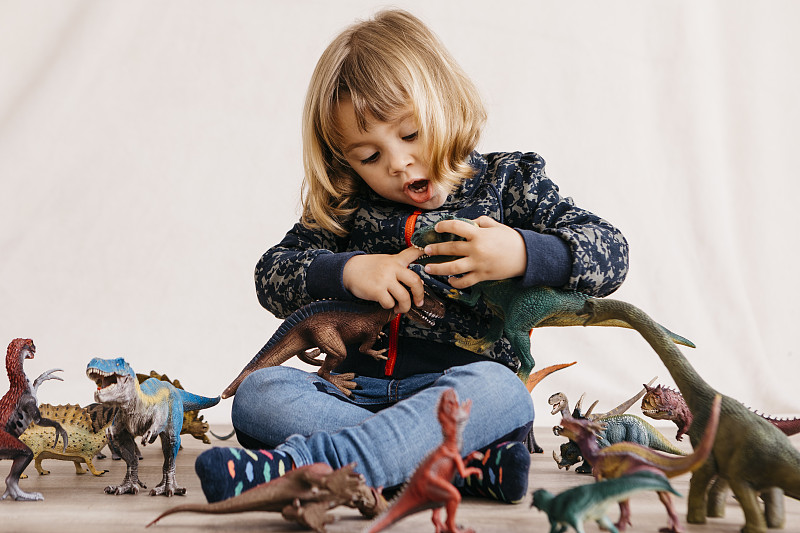 小女孩坐在地板上玩玩具恐龍的肖像圖片素材