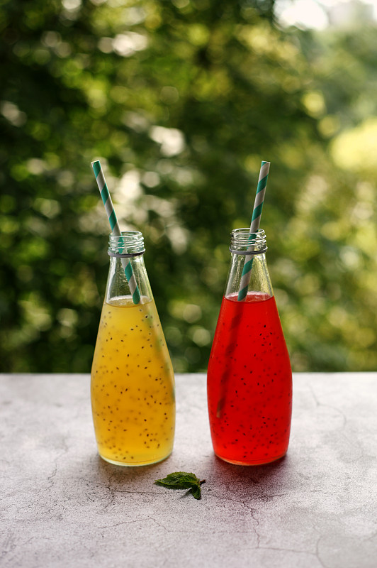 玻璃瓶與夏季飲料超級食物草莓和菠蘿汁與種子在綠樹的背景。垂直的照片。攝影圖片