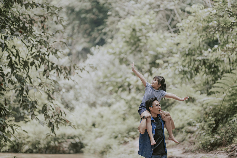 an asian chinese father carrying his daughter on shoulder in the jungle enjoying bonding time together at the river during weekend leisure time圖片素材