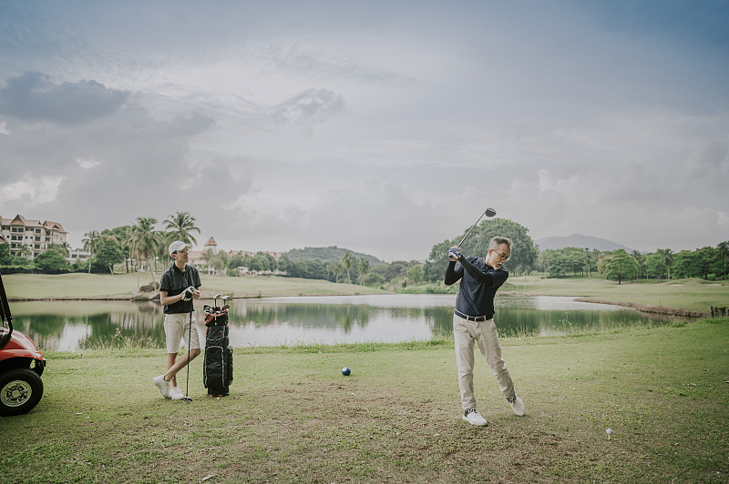 周末，一個成熟的亞洲華人在高爾夫球場揮桿，他的兒子在一旁觀看圖片素材