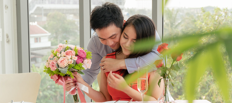 亞洲男人在情人節、周年紀念日或在餐館約會時擁抱女友并送花。男友驚喜的禮物。愛和歸屬感圖片下載