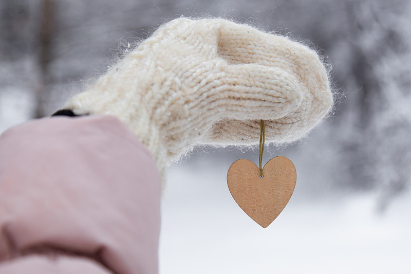 女人抱著木制的心在冬天的雪背景，近。情人節的概念圖片下載