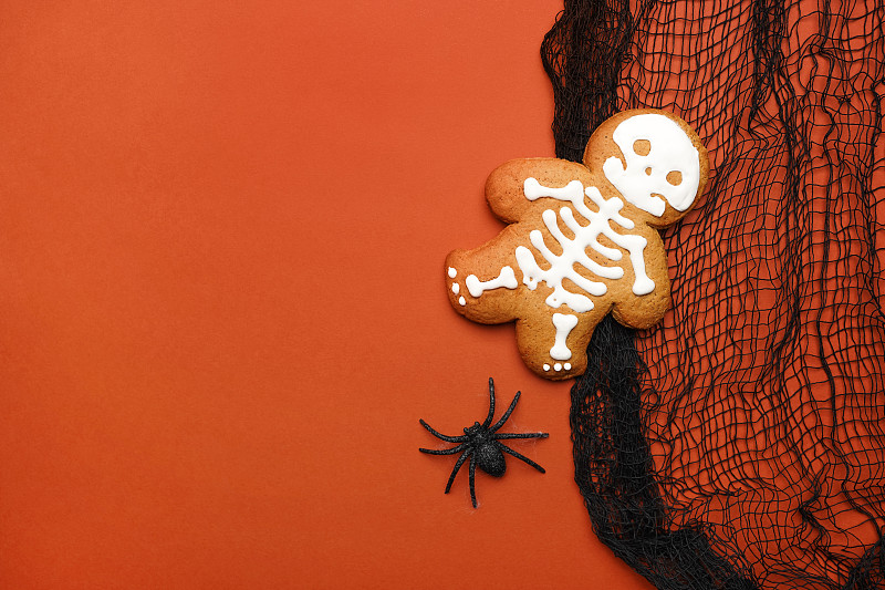 萬圣節背景由姜餅骨架蛋糕，黑色網布和閃閃發光的蜘蛛在橙色。萬圣節兒童裝飾概念?？植篮涂植烙腥さ谋尘芭c復制空間為您的設計攝影圖片