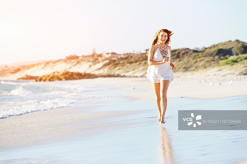 一个年轻女子在海滩上散步。一个年轻漂亮的女人沿着沙滩散步的肖像图片素材