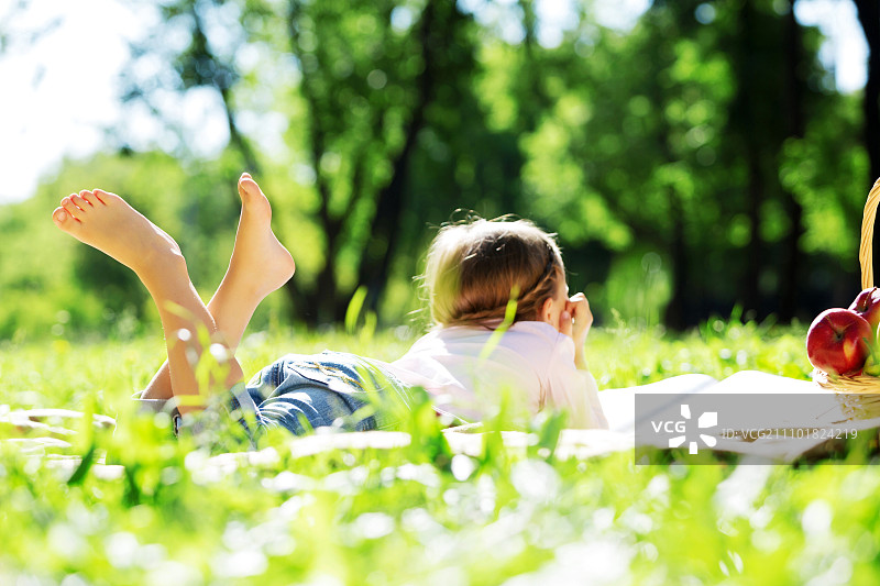 孩子躺在毯子上在夏天的公园野餐。女孩在公园图片素材
