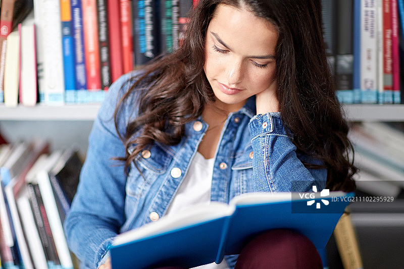 教育，高中，大学，学习和人的概念-近距离的学生女孩坐在图书馆的地板上看书图片素材