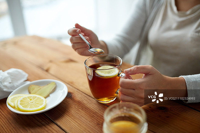 健康食品，饮食和民族科学概念-近距离观察妇女添加蜂蜜到茶杯与柠檬和生姜图片素材