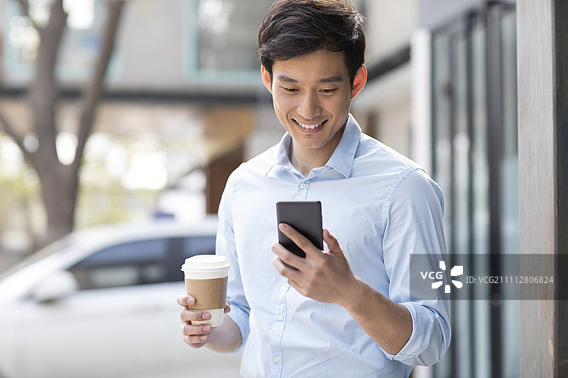 Young Chinese businessman with smart phone and coffee图片素材