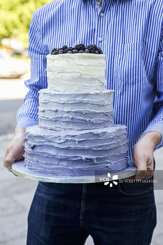 一个男人拿着一个三层的婚礼蛋糕图片素材