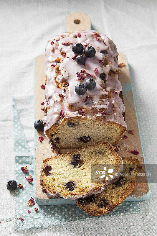 一个蓝莓切片面包蛋糕，上面有糖霜和干玫瑰花瓣图片素材