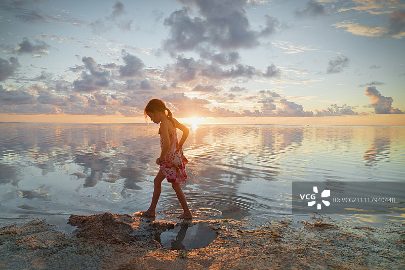 女孩涉水在平静的日落海滩冲浪图片素材