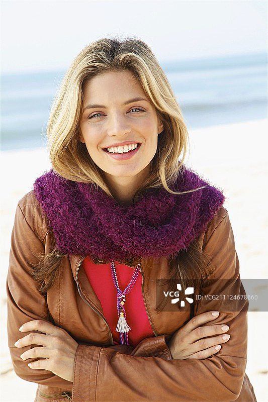 一个年轻的金发女人在海滩上穿着棕色皮夹克，粉色上衣和羊毛围巾图片素材