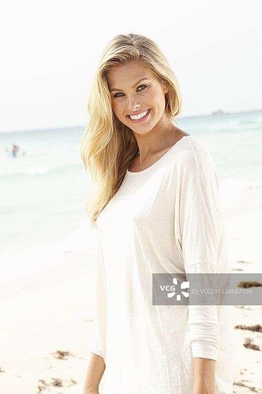 一个年轻的金发女人在沙滩上穿着一件白色的长衬衫图片素材