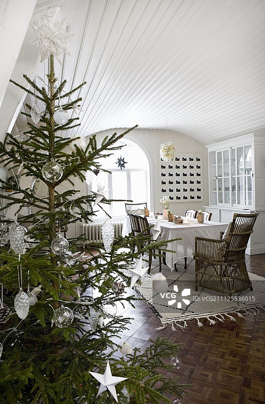 装饰着白色星星和玻璃小饰品的圣诞树;餐厅与木材覆盖，白色漆桶拱顶和马赛克拼花地板图片素材