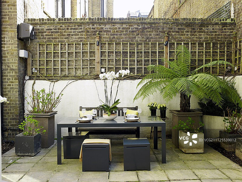 有遮蔽的砖墙庭院内的座位区;优雅的灰色凳子围绕着桌子，周围是盆栽植物图片素材