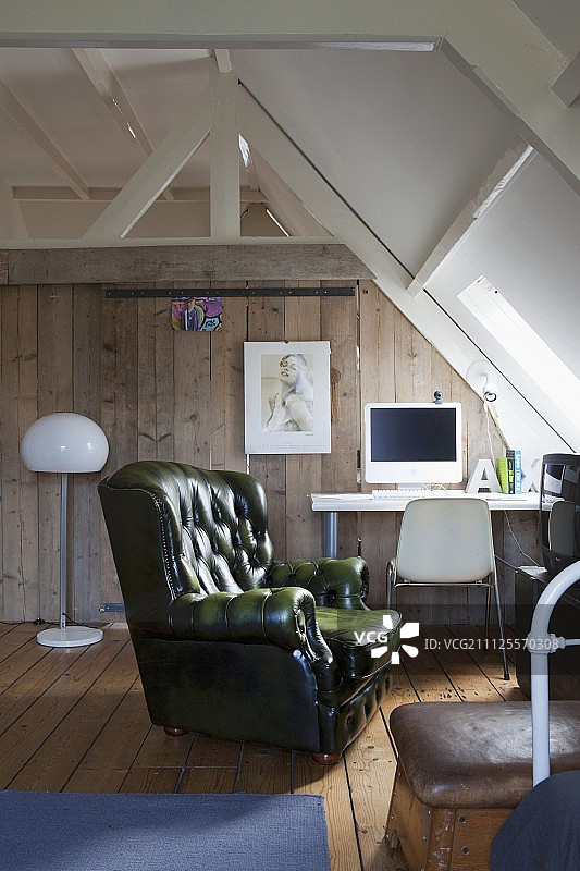 青少年阁楼房间里的绿色皮革躺椅;电脑放在桌子上，以木板墙为背景图片素材