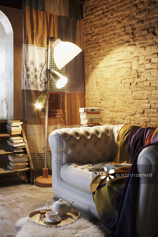 传统的扶手椅靠漆砖墙，一侧点亮标准灯，茶壶和茶杯盘在地板上，室内大气图片素材