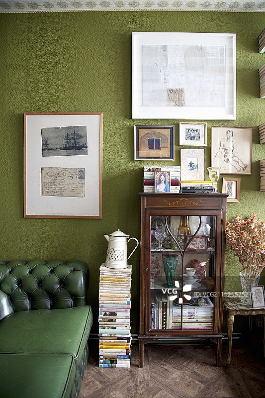 绿色的切斯特菲尔德沙发，古色古香的展示柜和绿色墙上的图片图片素材