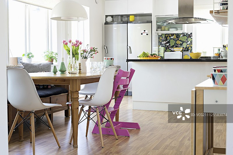 开放式厨房柜台前的木桌上摆放着经典的贝壳椅和粉红色的Tripp Trapp椅子图片素材