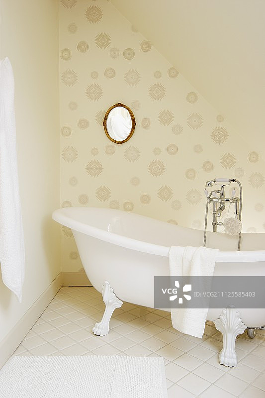 独立，爪足浴缸与老式水龙头配件在椭圆形镜子前的墙壁上与圆形图案墙纸图片素材