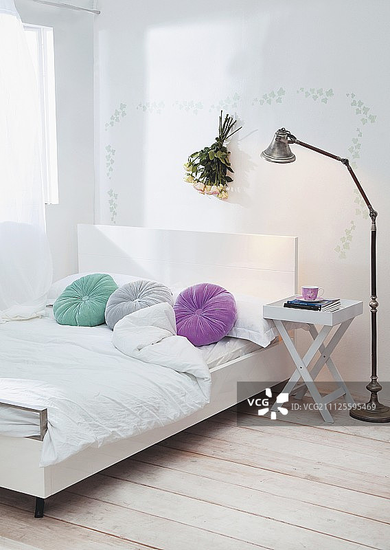 现代双人床配有白色床头板和圆形彩色散垫;折叠床头柜和复古标准灯图片素材