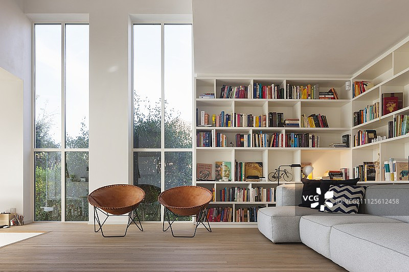 高窗前的复古皮壳椅、书柜和客厅里的灰色沙发图片素材