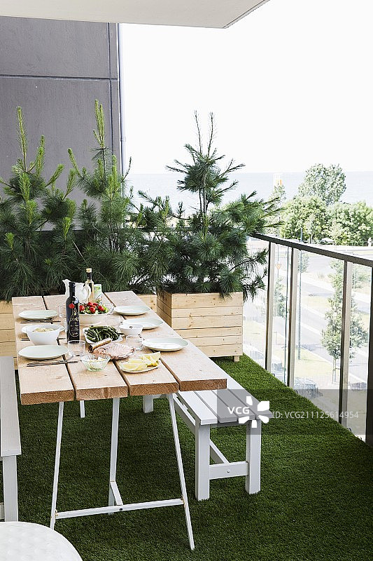 阳台设置桌子和白色长凳，人工草地板和小针叶树种植在木槽图片素材