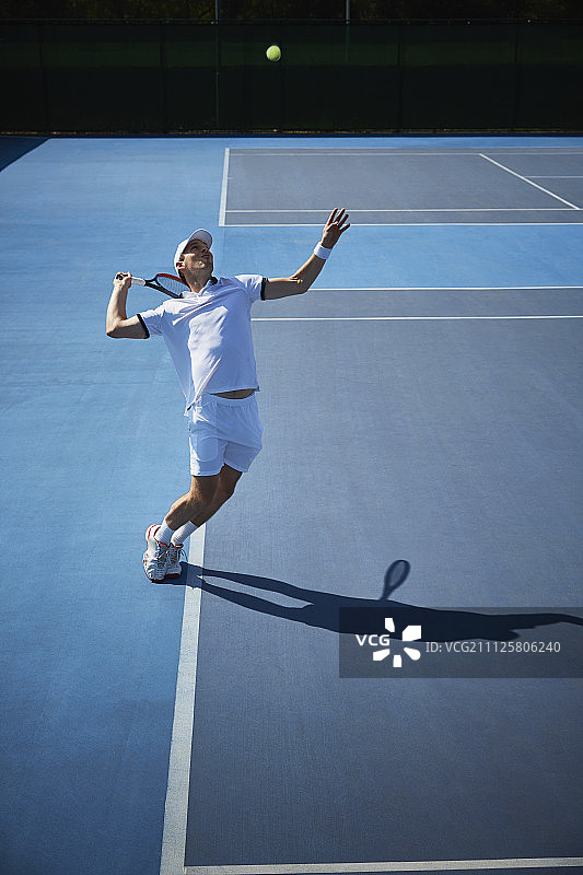 年轻的男子网球运动员在阳光明媚的蓝色网球场上打球图片素材