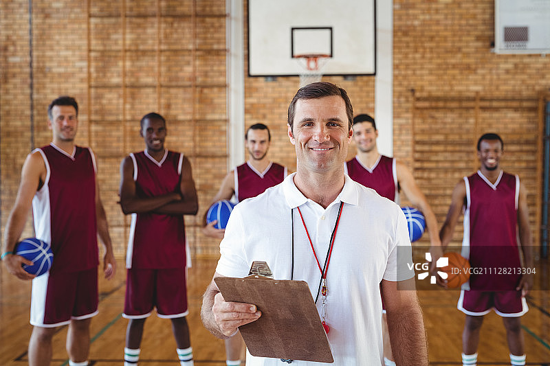 微笑的教练和篮球运动员站在球场上的肖像图片素材