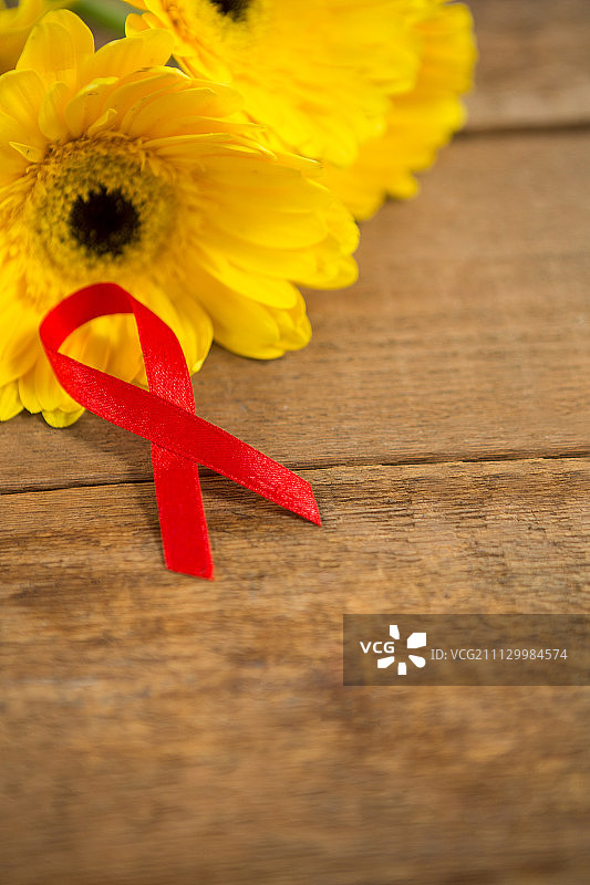 高角度的红色艾滋病意识丝带由非洲菊花木制桌子图片素材