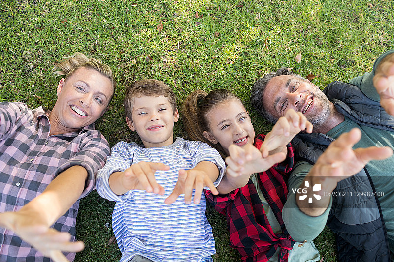 幸福的家庭躺在草地上，在公园里做手势图片素材