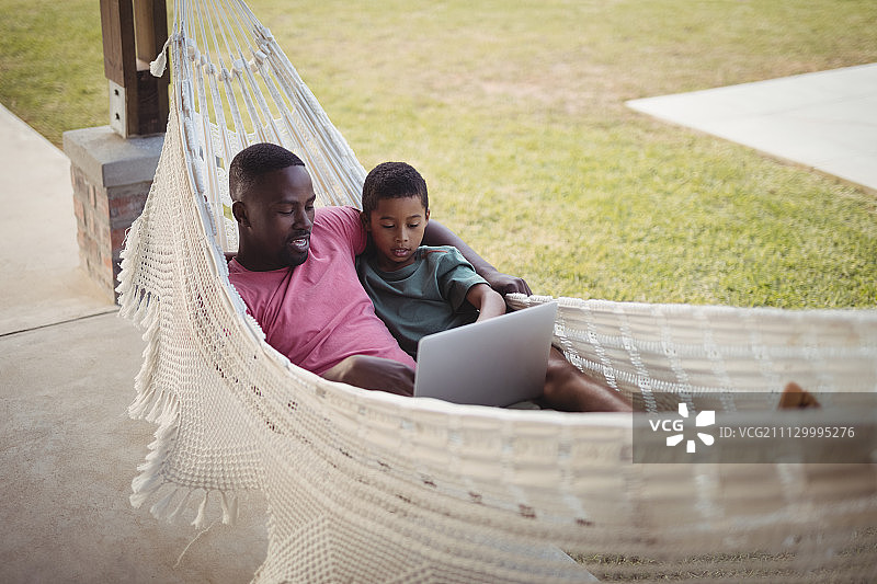 父亲和儿子在花园里的吊床上休息时使用笔记本电脑图片素材
