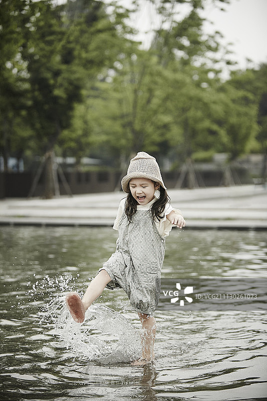 小女孩在公共公园的喷泉里玩耍和微笑图片素材