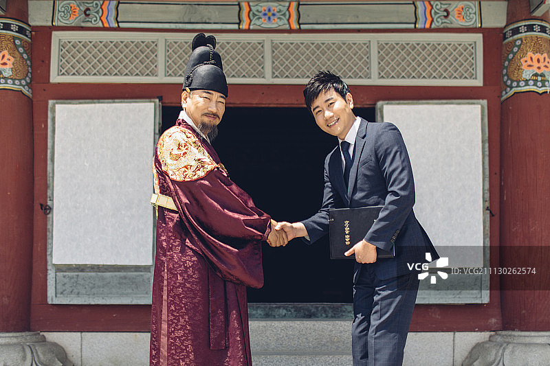 高级男子在韩国国王服装和现代年轻商人握着剪贴板握手图片素材