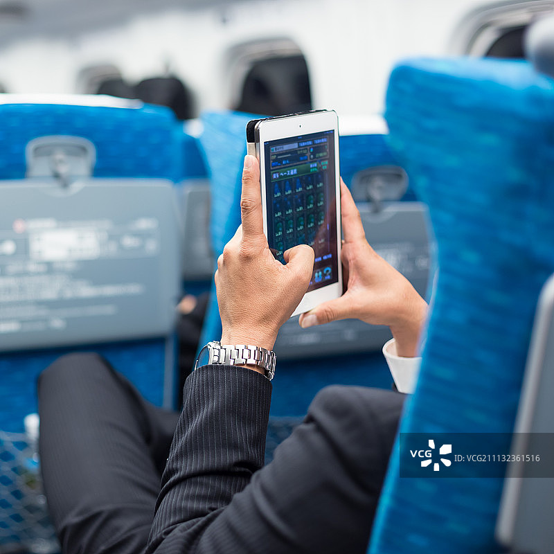 商人在飞机上使用平板手机。图片素材