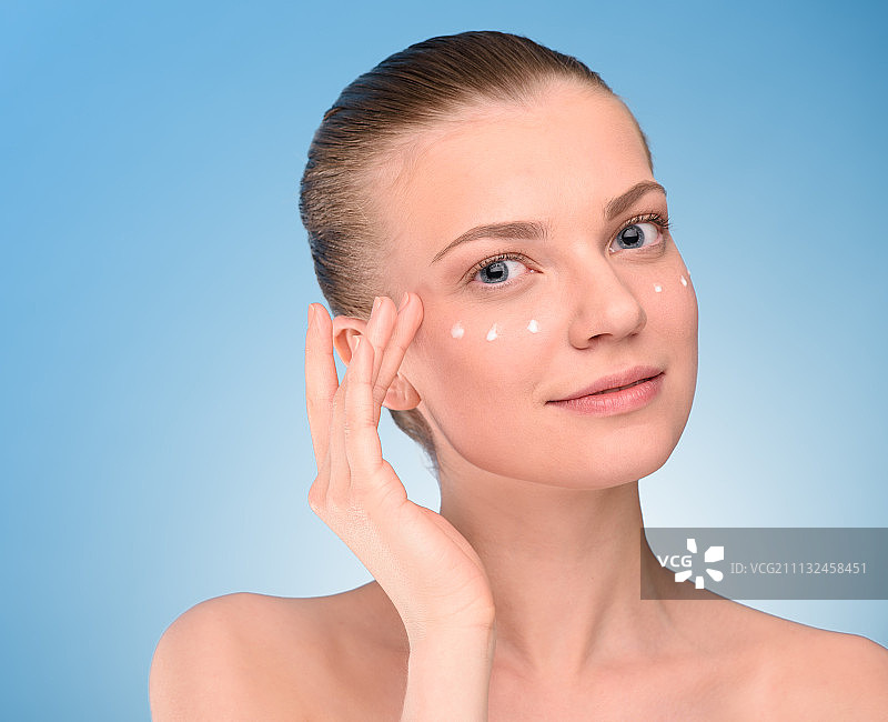 女士在脸上涂抹提拉霜，蓝色背景。图片素材