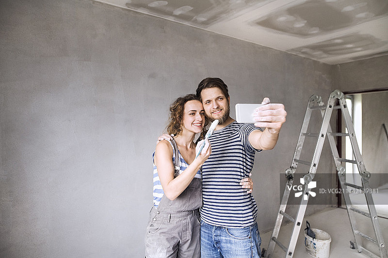 夫妇在家里刷墙，用智能手机自拍。图片素材