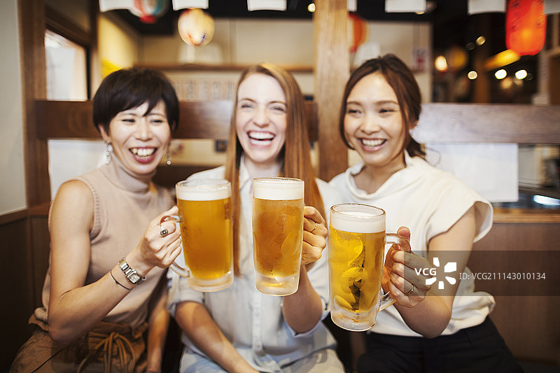 餐馆里，三个女人肩并肩坐在一张桌子旁，手里拿着大杯啤酒。图片素材