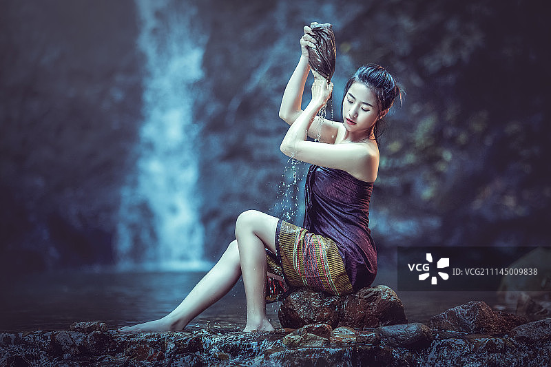 一个亚洲女人正在瀑布边洗澡。图片素材