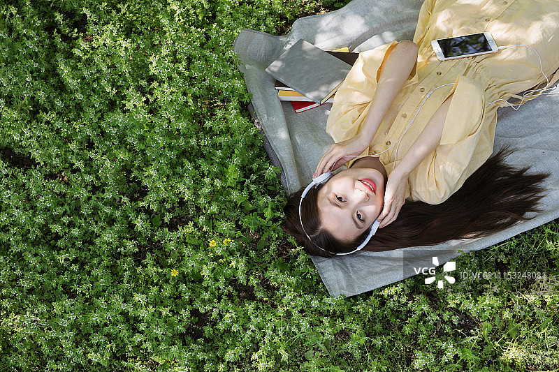 躺在草地上听歌的年轻女孩图片素材