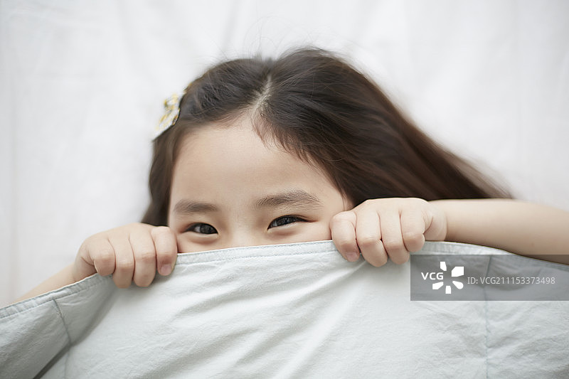 小女孩躺在床上躲避羽绒被的照片图片素材